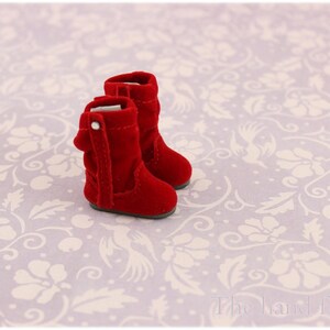 Puede incluir: Un par de botas de terciopelo rojo con punta puntiaguda y una hebilla en el lateral. Las botas est&aacute;n sobre un fondo blanco con un patr&oacute;n floral.