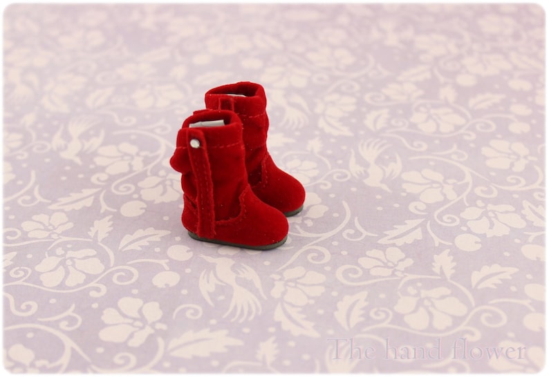 Puede incluir: Un par de botas de terciopelo rojo con punta puntiaguda y una hebilla en el lateral. Las botas est&aacute;n sobre un fondo blanco con un patr&oacute;n floral.