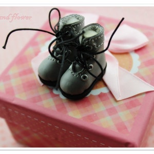 May include: A pair of gray miniature boots with black laces on a pink and white checkered gift box with a pink ribbon. The text "The hand flower" is written on the box.