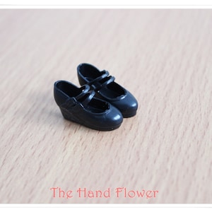 May include: A pair of black doll shoes with a wedge heel and two straps across the top.