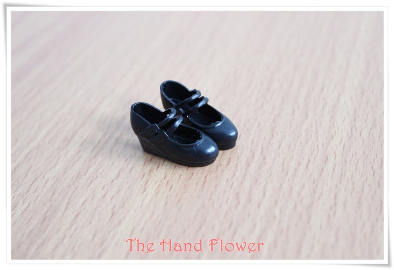 May include: A pair of black doll shoes with a wedge heel and two straps across the top.