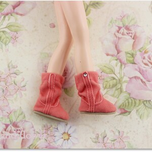 Puede incluir: Un par de botas de gamuza de color coral con un bot&oacute;n plateado en la parte superior de cada bota. Las botas est&aacute;n sobre un fondo floral.