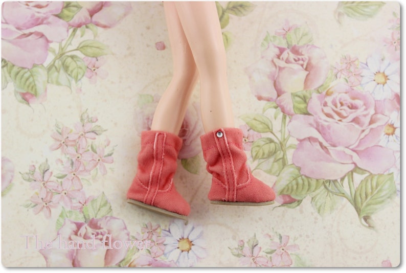 Puede incluir: Un par de botas de gamuza de color coral con un bot&oacute;n plateado en la parte superior de cada bota. Las botas est&aacute;n sobre un fondo floral.