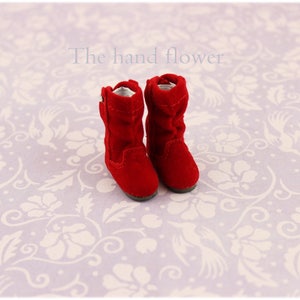 Puede incluir: Un par de botas de ante rojo con una cremallera en el lateral. Las botas est&aacute;n sobre un fondo blanco con un patr&oacute;n floral.