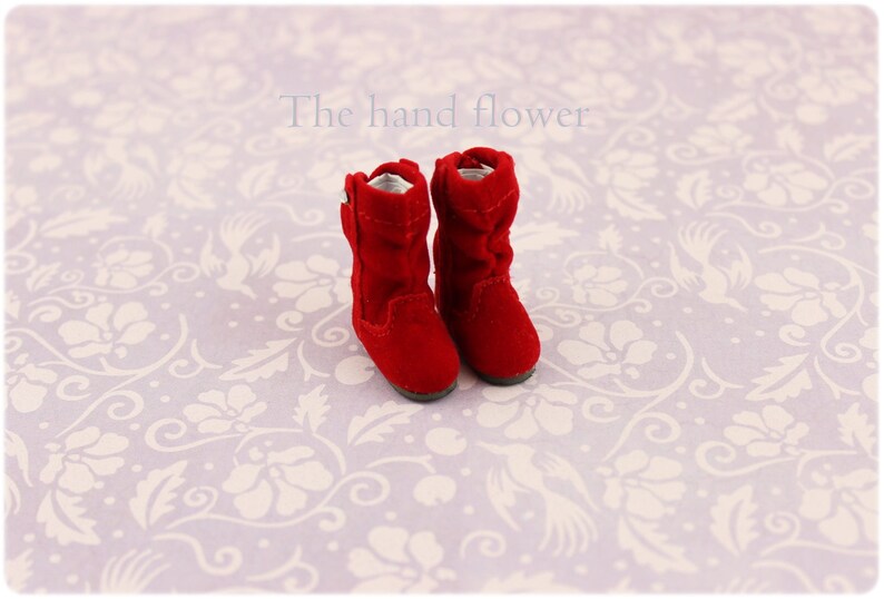 Puede incluir: Un par de botas de ante rojo con una cremallera en el lateral. Las botas est&aacute;n sobre un fondo blanco con un patr&oacute;n floral.