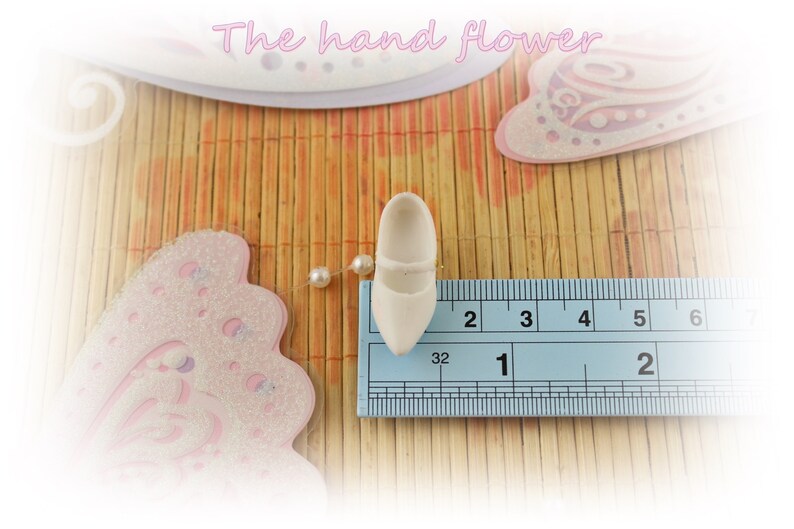 May include: A white ceramic shoe measuring 1 inch in length. The shoe is placed on a ruler for size reference.