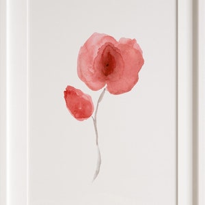 Può includere: Un dipinto ad acquerello incorniciato di un singolo papavero rosso con un bocciolo. Il dipinto è su uno sfondo bianco e ha una cornice bianca.
