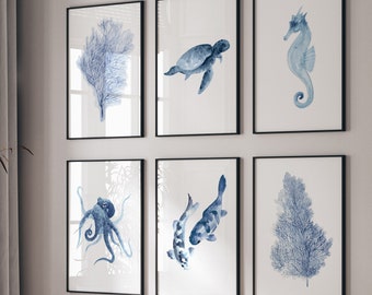 Puede incluir: Un conjunto de seis estampados acuarelados enmarcados que presentan ilustraciones azules y blancas de vida marina, incluyendo un pulpo, un caballito de mar, una tortuga y coral. Los estampados están dispuestos en un patrón de cuadrícula en una pared blanca.