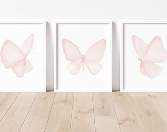 Puede incluir: Tres impresiones enmarcadas blancas con ilustraciones de mariposas de acuarela rosa. Las mariposas están en diferentes posiciones y tamaños.