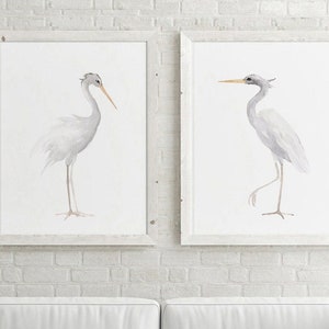 以下が含まれることがあります： 白いレンガの壁に、白いサギが左右を向いている水彩画が2枚額装されています。