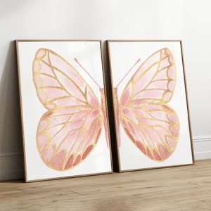 May include: Two framed prints of pink and gold butterflies. The butterflies are painted in a watercolor style with gold accents.