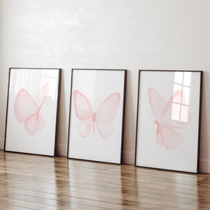 May include: Three framed prints with pink watercolor butterfly illustrations on a white background. The frames are black and the butterflies are different sizes and positions.