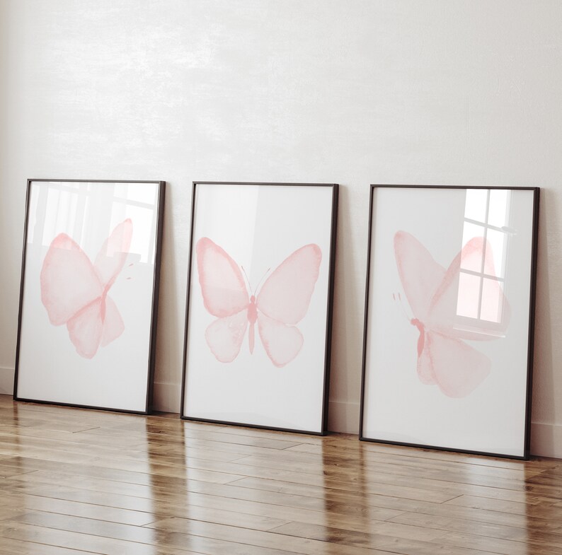 May include: Three framed prints with pink watercolor butterfly illustrations on a white background. The frames are black and the butterflies are different sizes and positions.
