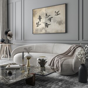 May include: A modern living room with a curved, off-white sofa, a marble coffee table, and a framed artwork depicting flying birds. Decorative items include a black vase, a gold candle holder, and a glass terrarium. The room has gray walls and a patterned rug.