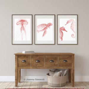 May include: Three framed watercolor prints of sea creatures in shades of pink. The prints feature a jellyfish, a sea turtle, and a seahorse.