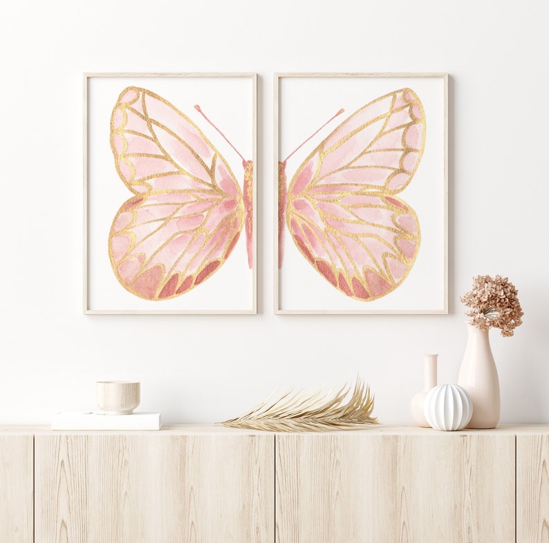 May include: Two framed prints of pink and gold butterflies with their wings spread open. The butterflies are set against a white background.