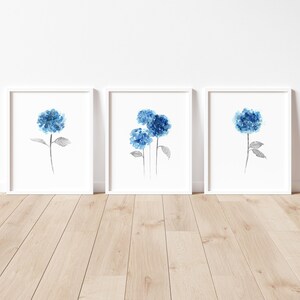 May include: Three framed watercolor paintings of blue hydrangeas on a white background. The hydrangeas are painted in shades of blue and gray.