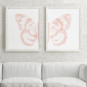 May include: Two framed prints of watercolor butterflies in a pale pink color. The butterflies are facing opposite directions and are set against a white background.