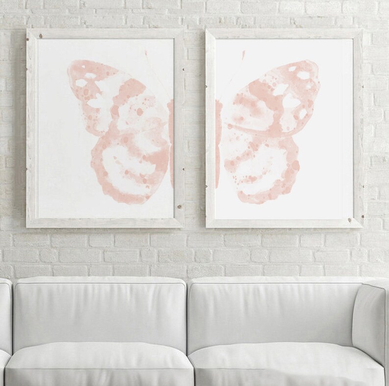 May include: Two framed prints of watercolor butterflies in a pale pink color. The butterflies are facing opposite directions and are set against a white background.