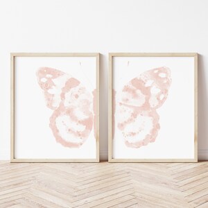 May include: A set of two framed prints featuring watercolor illustrations of pink butterflies. The butterflies are depicted with their wings spread open, showcasing intricate details and a delicate, faded appearance.