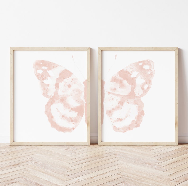 May include: A set of two framed prints featuring watercolor illustrations of pink butterflies. The butterflies are depicted with their wings spread open, showcasing intricate details and a delicate, faded appearance.
