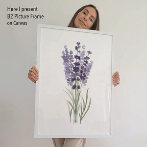 May include: A white picture frame with a watercolor painting of lavender flowers. The frame is being held by a person.