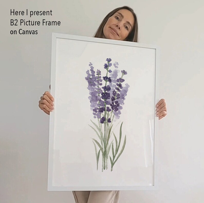 May include: A white picture frame with a watercolor painting of lavender flowers. The frame is being held by a person.