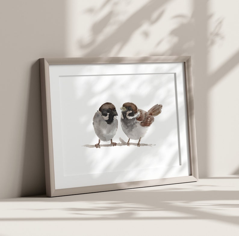 May include: A framed watercolor painting of two brown sparrows perched on a branch. The sparrows are facing each other, with one looking to the left and the other looking to the right. The painting is set against a white background.