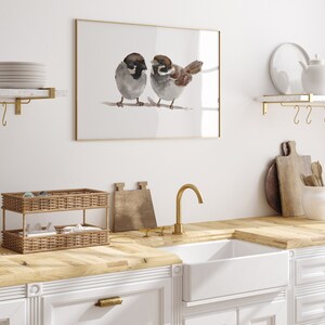 May include: A framed watercolor painting of two brown and gray sparrows perched on a branch. The painting is hanging on a white wall above a kitchen sink with a gold faucet.
