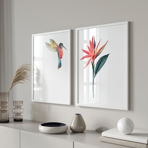 May include: Two framed watercolor paintings, one depicting a hummingbird in flight and the other a red and green tropical flower.
