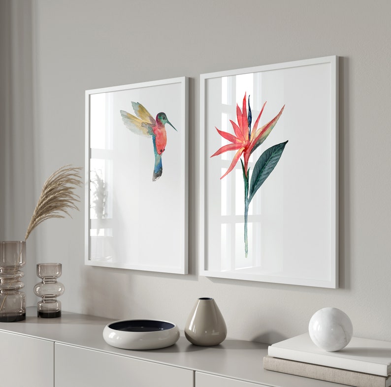 May include: Two framed watercolor paintings, one depicting a hummingbird in flight and the other a red and green tropical flower.