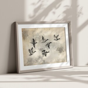 May include: Framed art print featuring a watercolor painting of six ducks in flight. The artwork has a neutral color palette with shades of gray, beige, and white. The ducks are depicted with dark gray and black details against a cloudy background.