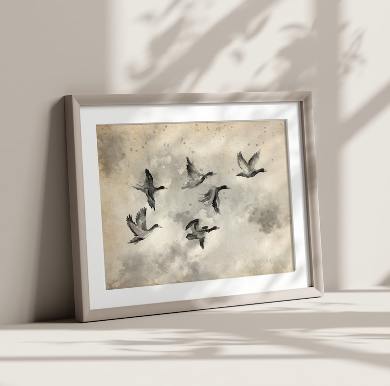 May include: Framed art print featuring a watercolor painting of six ducks in flight. The artwork has a neutral color palette with shades of gray, beige, and white. The ducks are depicted with dark gray and black details against a cloudy background.