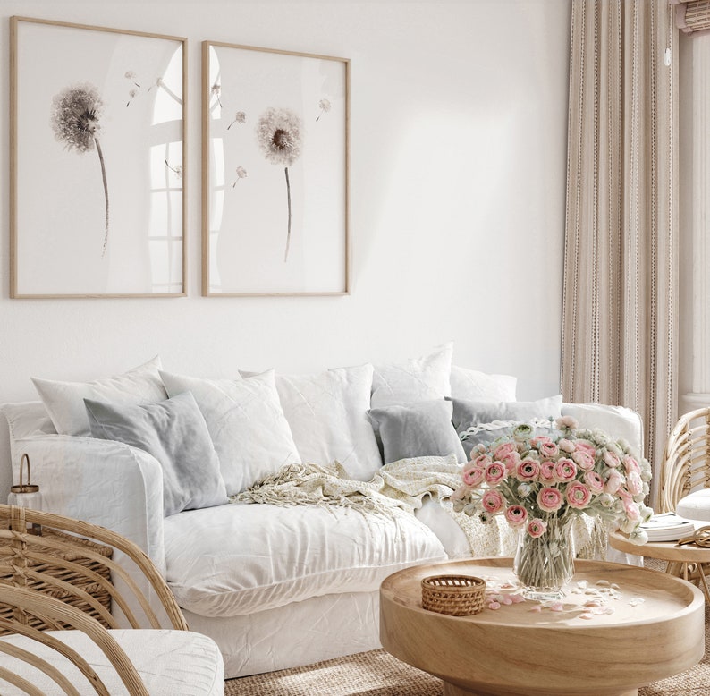 May include: A white couch with a throw blanket and pillows, a wooden coffee table with a vase of pink flowers, and two framed prints of dandelion flowers on the wall.