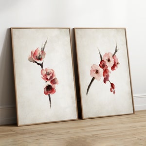 May include: Two framed watercolor paintings of pink and red cherry blossoms on a branch. The paintings are on a light brown wood floor.