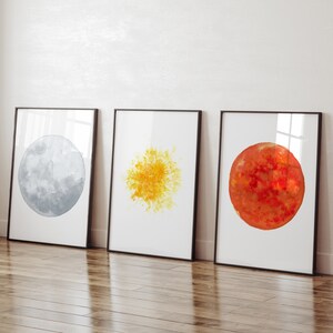 May include: Three framed watercolor paintings of celestial bodies. The first painting is a gray moon, the second is a yellow sun, and the third is a red planet.