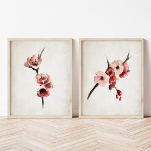 May include: Two framed watercolor paintings of pink cherry blossoms on a branch. The paintings are on a white background and have a light wood frame.