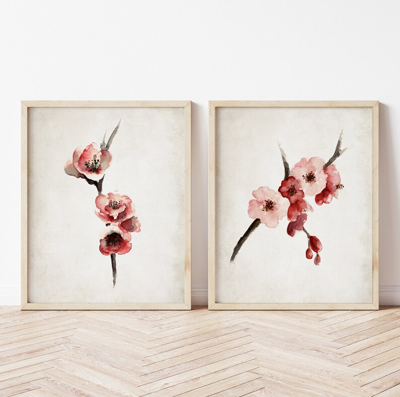 May include: Two framed watercolor paintings of pink cherry blossoms on a branch. The paintings are on a white background and have a light wood frame.
