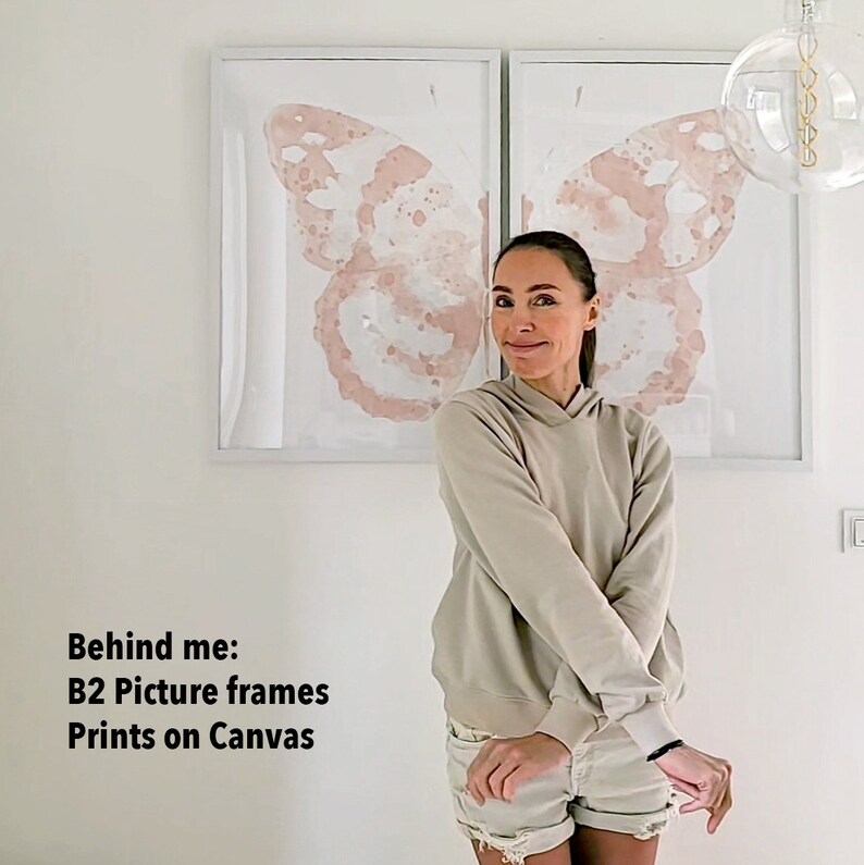 May include: Two large framed prints of a watercolor butterfly design on canvas. The prints are in a white frame and are hanging on a white wall. A person is standing in front of the prints.