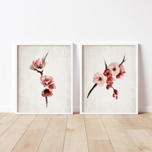 May include: Two framed watercolor paintings of delicate pink and red blossoms on a branch. The paintings are on a white background and are framed in white.