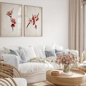 May include: A white couch with pillows and a throw blanket, a wooden coffee table with a vase of pink flowers, and two framed watercolor paintings of pink flowers on a white wall.