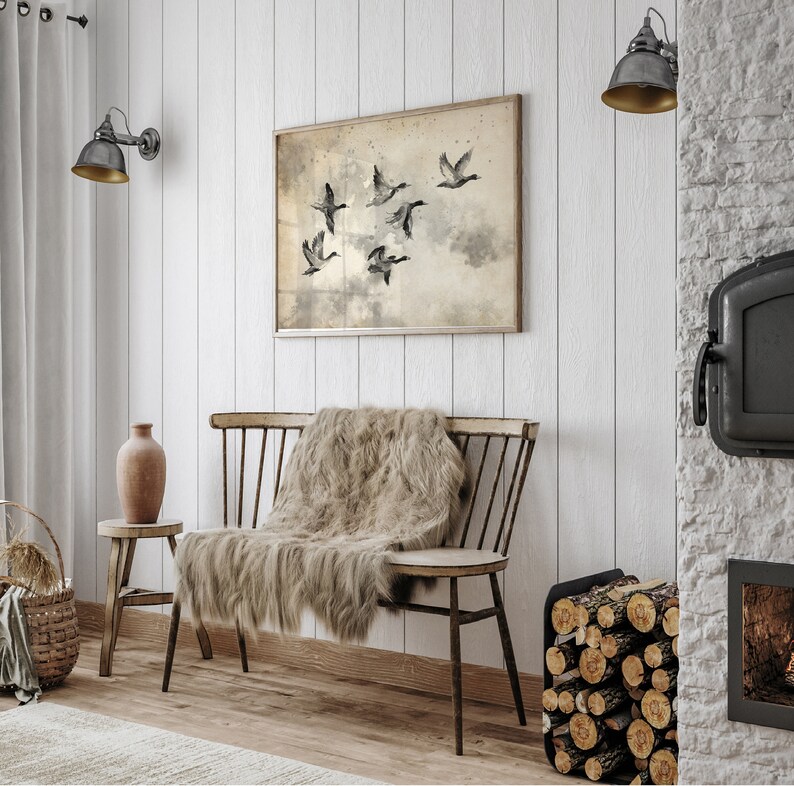 May include: A rustic interior scene featuring a wooden bench with a faux fur throw, a small side table with a vase, and a framed artwork depicting flying birds. The walls are white, and the scene is illuminated by wall-mounted lamps.
