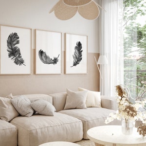 K&ouml;nnte beinhalten: Drei gerahmte Schwarzwei&szlig;-Aquarell-Federdrucke an einer beigefarbenen Wand &uuml;ber einem hellbeigen Ecksofa mit Kissen. Eine Vase mit Trockenblumen steht auf einem runden wei&szlig;en Couchtisch.