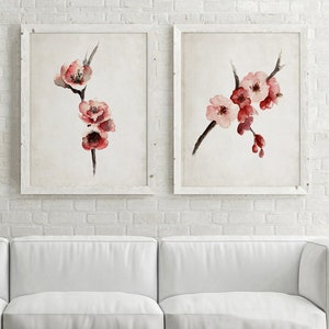 May include: Two framed watercolor paintings of pink and red blossoms on branches. The paintings are hung on a white brick wall above a white couch.