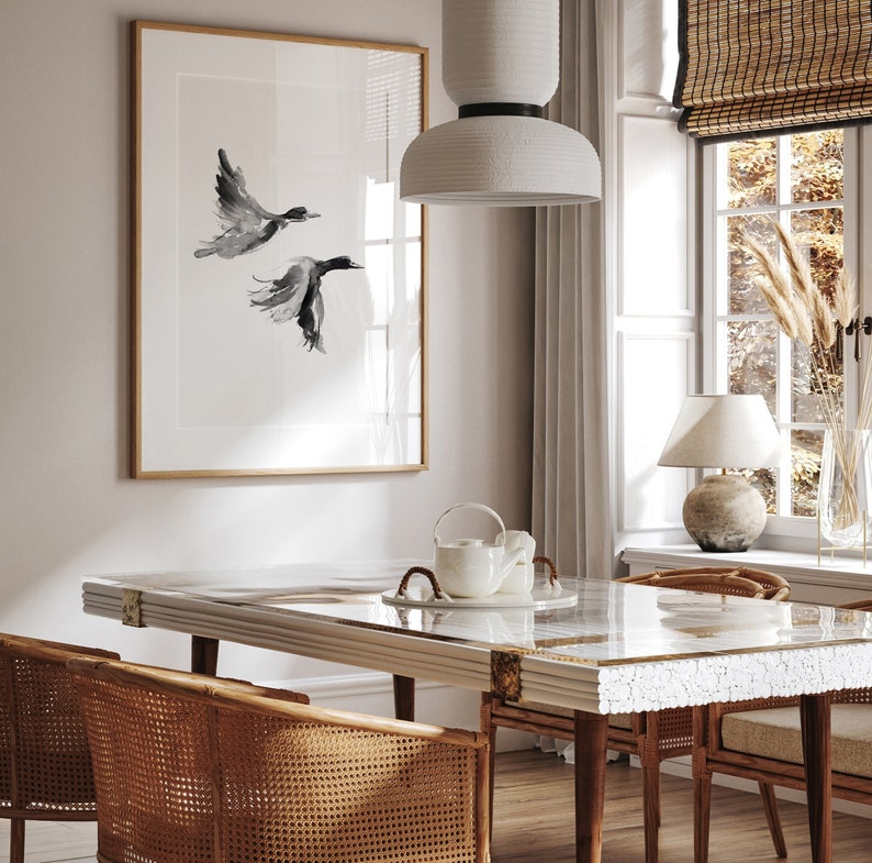 May include: A white dining table with a glass top and a white ceramic teapot on the table. The table is surrounded by four wicker chairs. A framed black and white print of two birds in flight hangs on the wall behind the table.