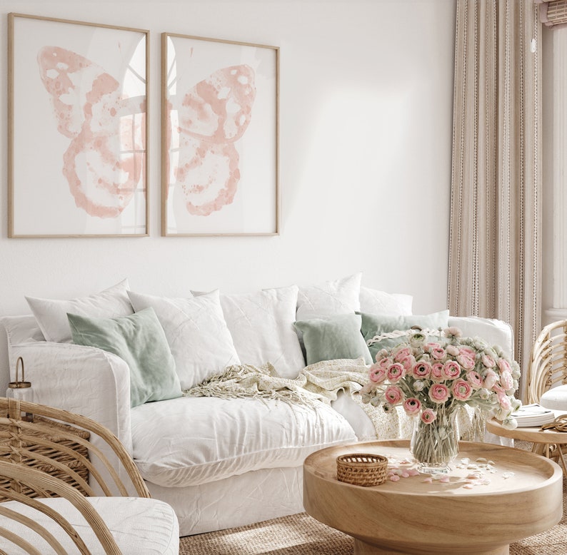 May include: A white couch with pillows and a throw blanket in a living room setting. A vase of pink flowers sits on a wooden coffee table with a woven basket.