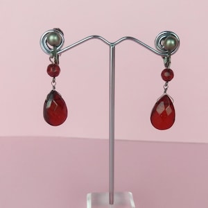 May include: A pair of red teardrop-shaped clip-on earrings with silver accents.