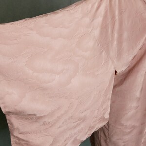 May include: A pale pink kimono with a subtle cloud pattern. The kimono is made of a soft, silky fabric and has a relaxed fit.