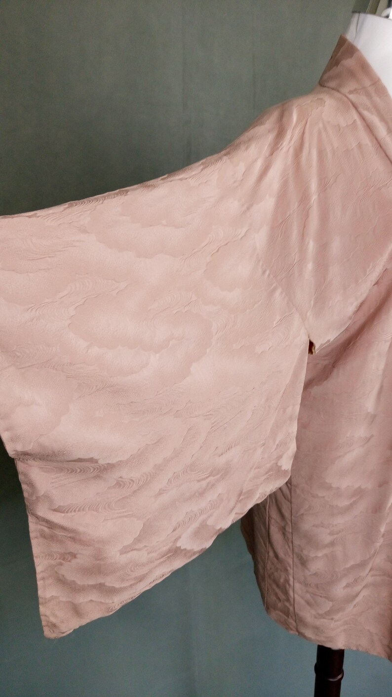 May include: A pale pink kimono with a subtle cloud pattern. The kimono is made of a soft, silky fabric and has a relaxed fit.