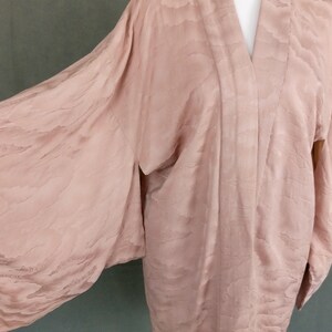 May include: A pale pink kimono with a subtle cloud pattern. The kimono is made of a soft, silky fabric and has long, wide sleeves.